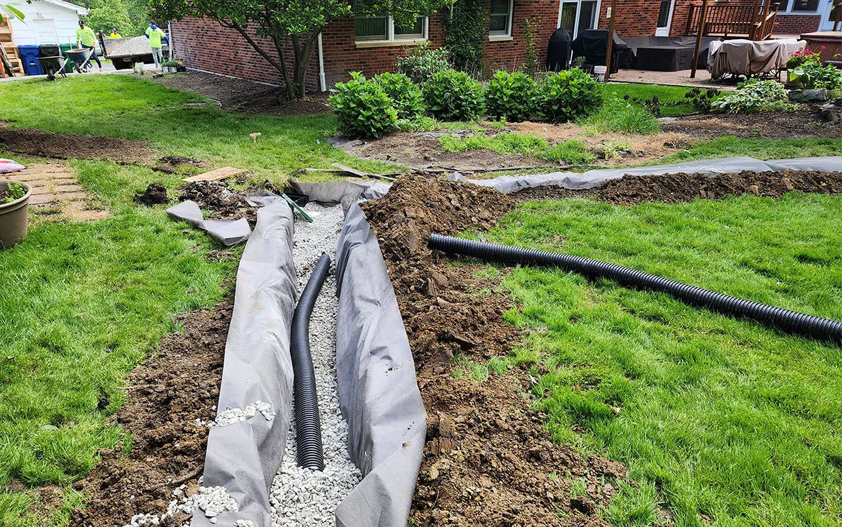 French drain trench with landscape fabric, gravel, and perforated pipe being installed in a Chicagoland backyard